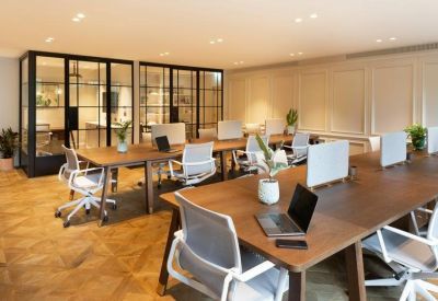 Co-working space with long wooden desks, ergonomic chairs, and glass partitions.