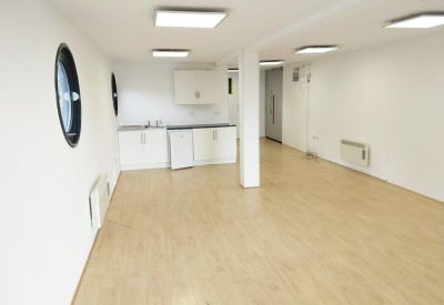 Bright communal kitchen and breakout area with light wood flooring and porthole windows.