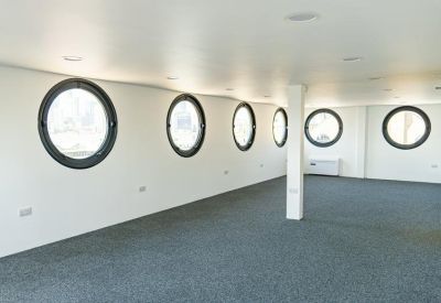 Spacious open-plan office space with grey carpeting and distinctive round porthole windows.