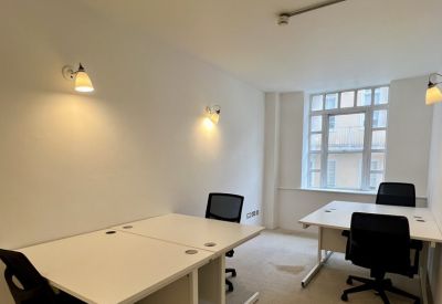 Private four-desk office suite with white walls and natural light from a large window.