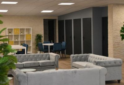 Spacious communal lounge with grey tufted sofas and indoor plants.