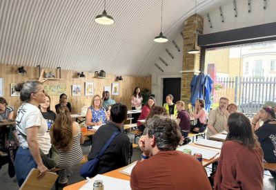 Large group gathering in a communal workshop space with industrial arched ceiling.