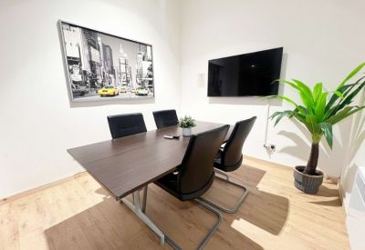 Private meeting room with a dark wood table, four chairs, and a wall-mounted TV.