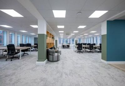 Sunlit coworking space with rows of black office chairs and green accent pillars.