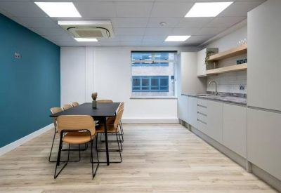Contemporary office kitchen and dining area with light wood flooring and teal feature wall.