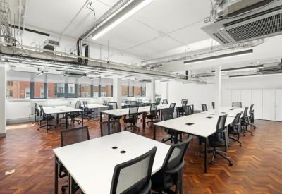 Open-plan workspace featuring rows of white desks, black chairs, and exposed ceiling ductwork.
