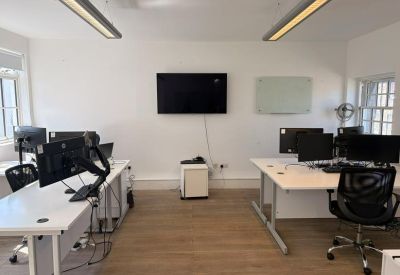 Bright coworking area with workstations, a wall-mounted TV, and light wood flooring.