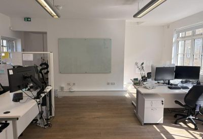 Clean office area featuring white desks, black ergonomic chairs, and a large whiteboard.