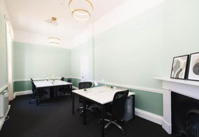 Bright office with two white desks, black chairs, and light green accent walls.