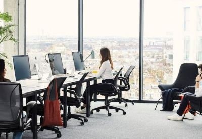 Bright open-plan office with rows of workstations and floor-to-ceiling windows overlooking the city.