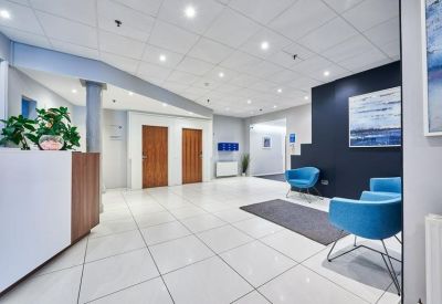 Modern reception lobby with white tiled floors, blue armchairs, and wood-paneled accents.