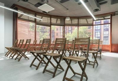 Auditorium-style meeting space with rows of wooden folding chairs and large windows.