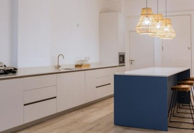Modern communal kitchen with a blue island, wooden bar stools, and wicker pendant lights.