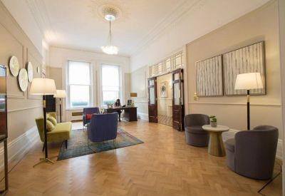 Spacious reception lounge with parquet flooring, colorful armchairs, and bright windows.