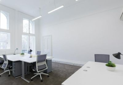 Bright open-plan office with white desks, grey chairs, and high ceilings.