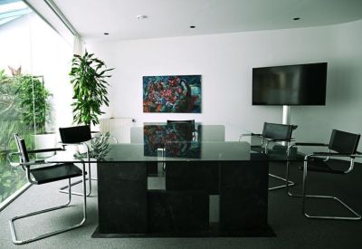 Professional meeting room with a large black glass table and wall-mounted screen.