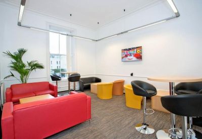 Modern breakout lounge with red sofas, yellow armchairs, and a wall-mounted TV.