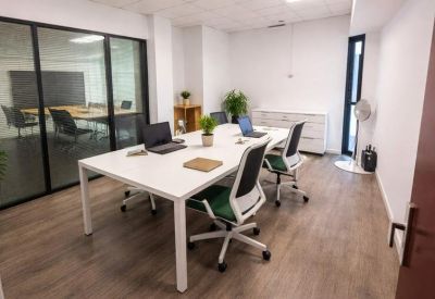 Bright four-person meeting table with laptops and glass-walled office in the background.