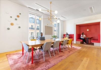 Long communal wooden table on a pink rug with a modern gold light fixture and red seating nook.