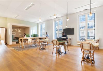 Bright workspace featuring round cafe tables, wicker chairs, and a wall-mounted television.