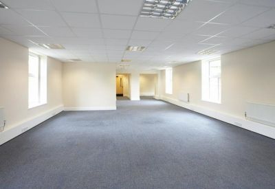 Large empty open-plan office suite with grey carpeting and bright windows.