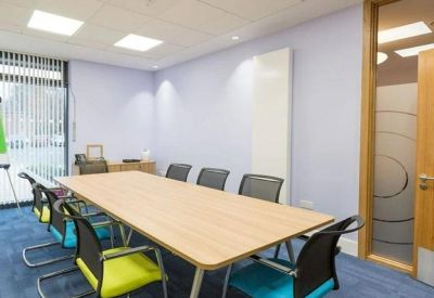 Meeting room with a light wood table and vibrant teal and lime green chairs.