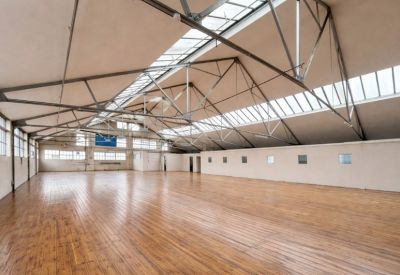 Expansive industrial loft with polished wood flooring and exposed steel roof trusses under skylights.