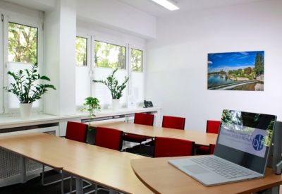 Classroom-style training room with red chairs, wooden tables, and potted plants by the windows.
