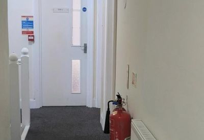 Narrow carpeted hallway leading to a white office door with a fire extinguisher.