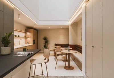 Bright communal lounge and kitchen area with light wood finishes, a long banquette, and a central skylight.