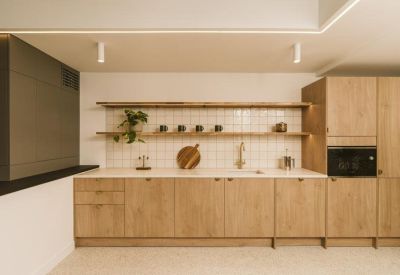 Modern office kitchen with natural wood cabinetry, floating shelves, and integrated appliances.