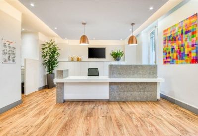 Clean white reception desk with wood flooring, colorful wall art, and hanging lamps.
