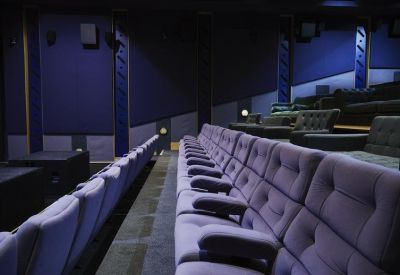 Private cinema room featuring tiered rows of purple velvet seating and blue acoustic wall panels.