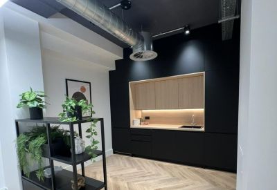 Sleek communal kitchen with black cabinetry, wood accents, and potted plants.