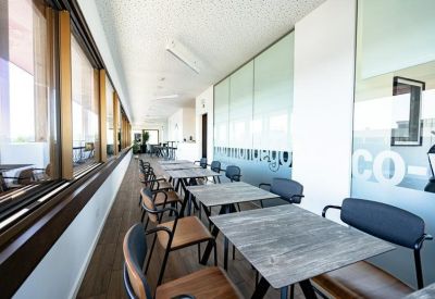 Indoor dining area with small wooden tables and black chairs alongside a glass wall.