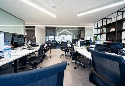 Large open-plan office with white desks, ergonomic black chairs, and glass partitions.
