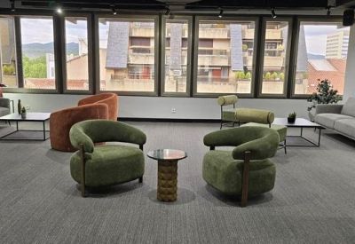 Spacious communal lounge area with green and orange velvet armchairs and grey sofas.