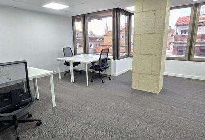 Bright corner office suite with white desks, black chairs, and large windows.