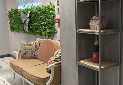 Reception lobby featuring a plush tan loveseat, floral cushions, and a green hedge feature wall.