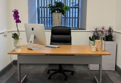 Private office workspace with a wooden desk, black leather chair, and a large window with bars.