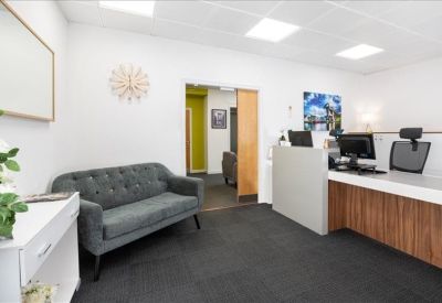 Reception area featuring a wood-fronted desk, grey tufted sofa, and wall-mounted art.