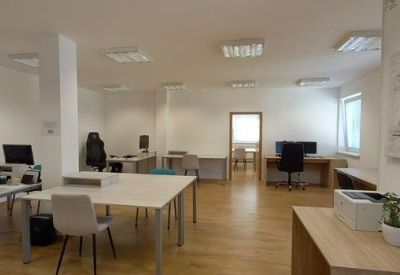 Spacious open-plan office with multiple desks, computer monitors, and a central white table.
