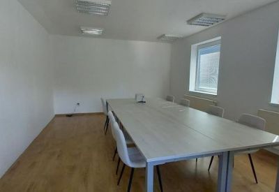Conference room with a long rectangular table, grey chairs, and bright windows.