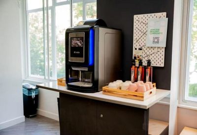 Modern coffee station with a professional espresso machine and flavored syrups in a bright communal area.