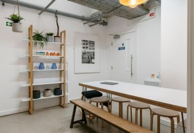Communal dining area with wooden shelving, potted plants, and a long white table with stools.