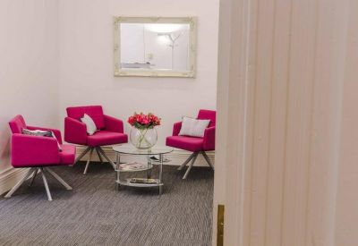 Lounge area with bright pink velvet armchairs and a glass coffee table.