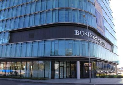 Glass-walled entrance with building signage and street lamp.