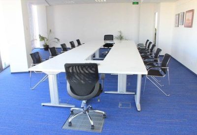 Bright conference room with a long white table and blue carpeting.