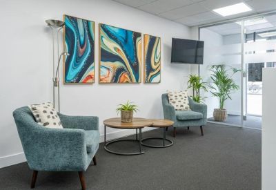 Casual waiting area with blue armchairs, abstract wall art, and indoor plants.