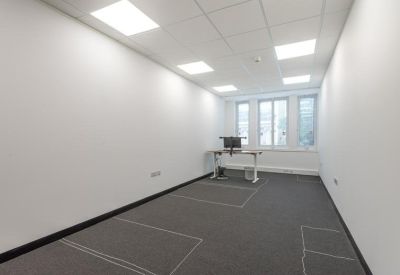 Spacious private office with grey carpeting and a standing desk by the window.